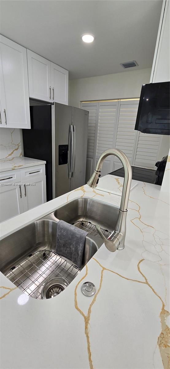 kitchen featuring white cabinets, light stone counters, stainless steel fridge with ice dispenser, and tasteful backsplash