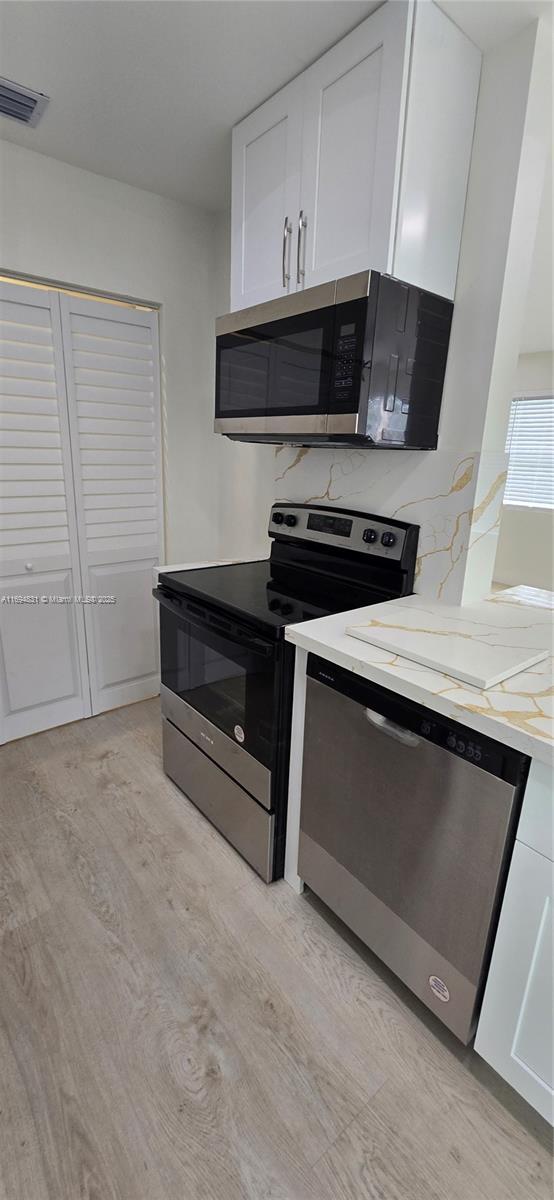 kitchen featuring light stone countertops, light hardwood / wood-style flooring, white cabinets, and appliances with stainless steel finishes