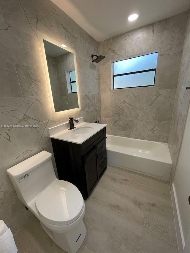 full bathroom featuring tiled shower / bath combo, toilet, tile walls, and vanity