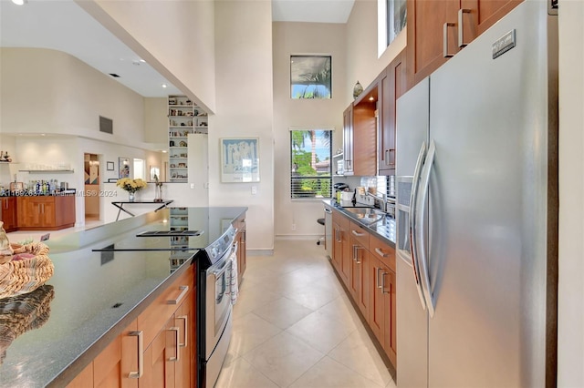 kitchen featuring light tile patterned floors, a towering ceiling, stainless steel appliances, and dark stone countertops