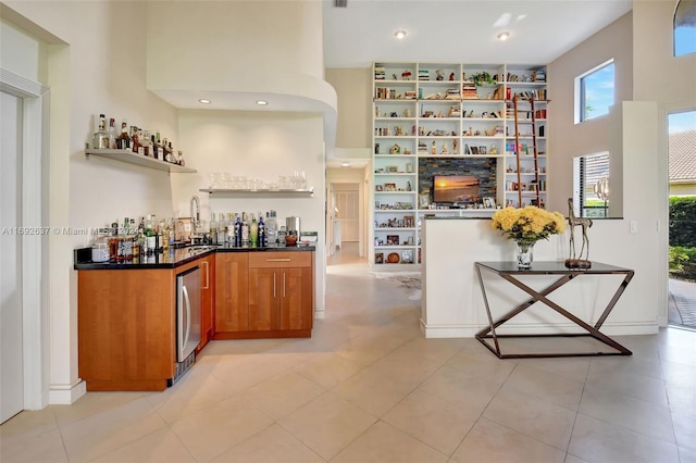 bar featuring stainless steel refrigerator, sink, a towering ceiling, and light tile patterned floors