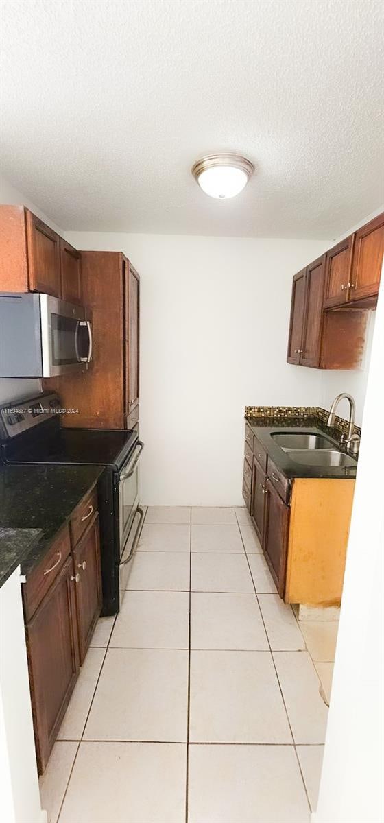 kitchen with light tile patterned floors, black range with electric cooktop, a textured ceiling, and sink