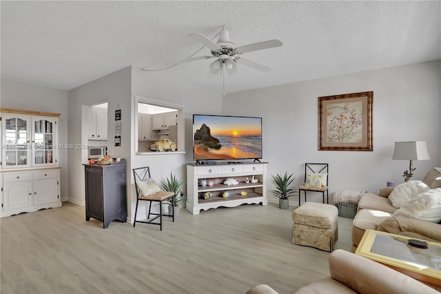 living room featuring ceiling fan, a textured ceiling, and light wood-type flooring