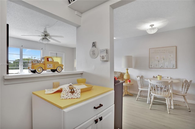 kitchen with ceiling fan, light wood-type flooring, white cabinetry, and a textured ceiling