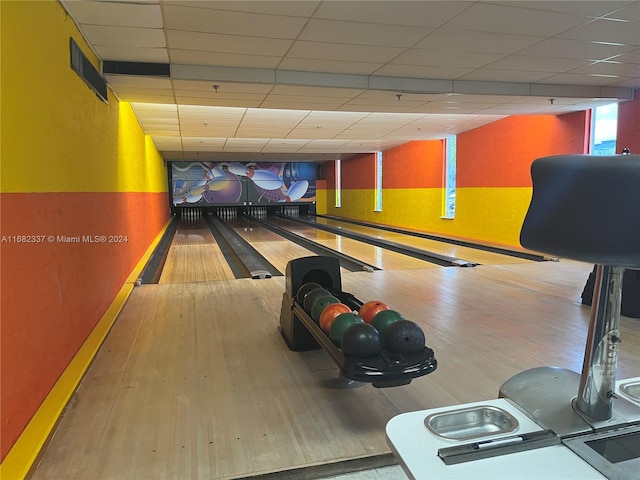 rec room with light wood-type flooring, a bowling alley, and a paneled ceiling