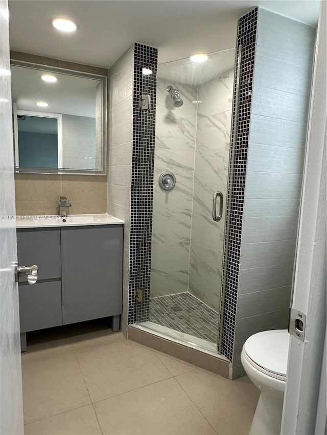 bathroom featuring tile patterned floors, toilet, a shower with door, vanity, and tile walls