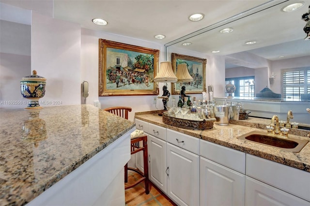 kitchen with light hardwood / wood-style floors, light stone countertops, white cabinetry, and sink