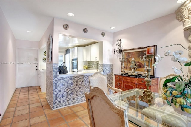 interior space featuring kitchen peninsula, light tile patterned floors, decorative backsplash, and stainless steel oven