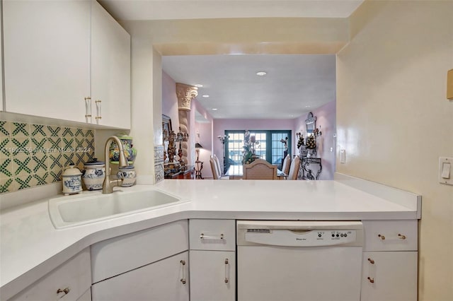 kitchen with backsplash, white dishwasher, white cabinets, sink, and kitchen peninsula