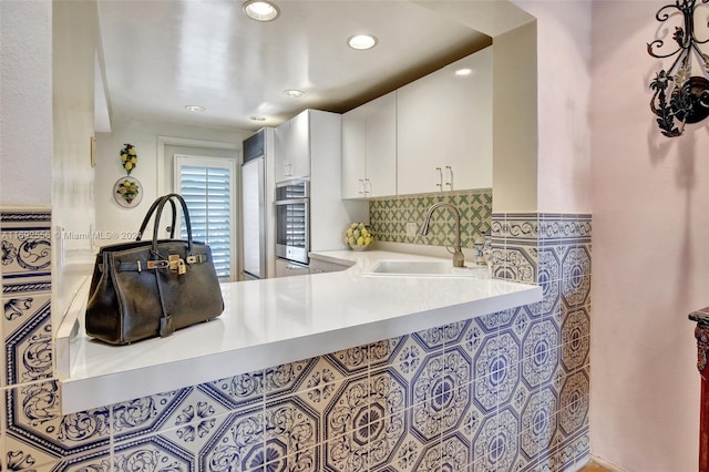 kitchen featuring kitchen peninsula, white cabinetry, sink, and tasteful backsplash