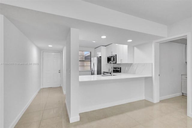 kitchen with white cabinetry, kitchen peninsula, appliances with stainless steel finishes, decorative backsplash, and sink