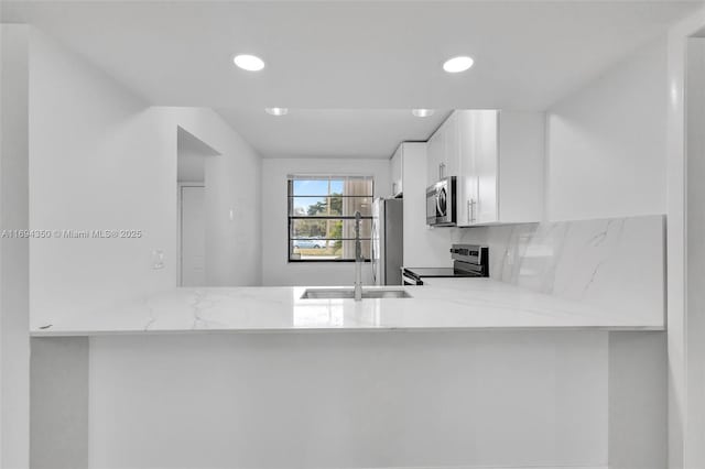 kitchen featuring kitchen peninsula, stainless steel appliances, white cabinetry, and light stone countertops