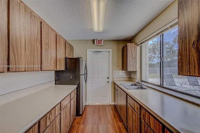 kitchen featuring a textured ceiling, backsplash, stainless steel refrigerator, and sink