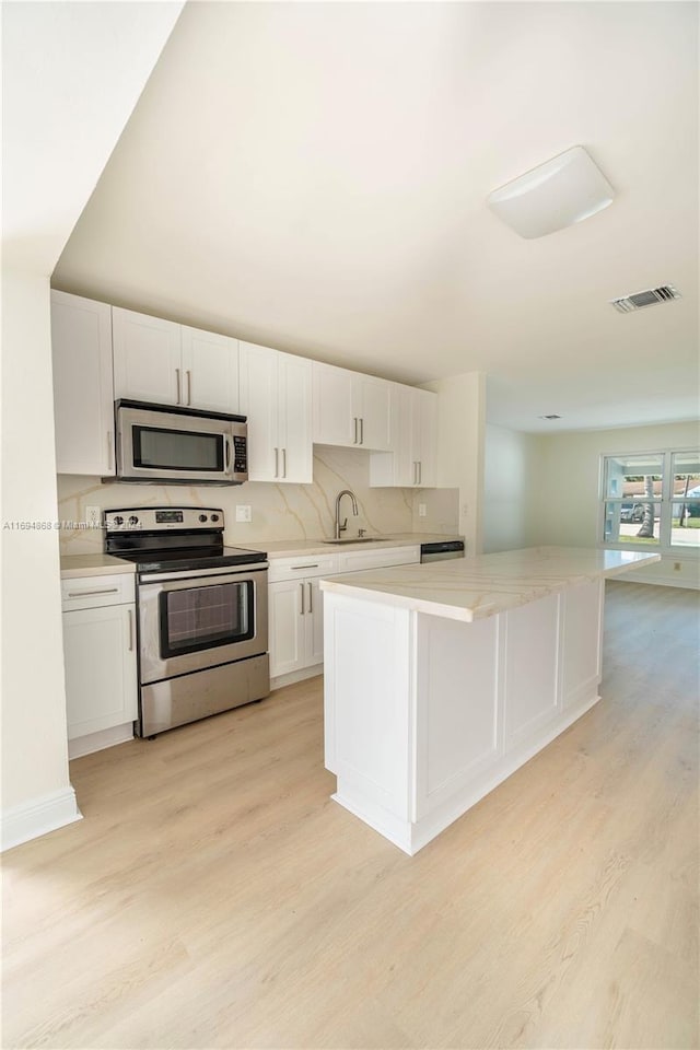 kitchen with sink, white cabinets, stainless steel appliances, and light wood-type flooring