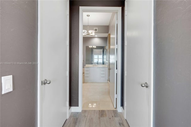 hallway with light hardwood / wood-style flooring, a chandelier, and sink