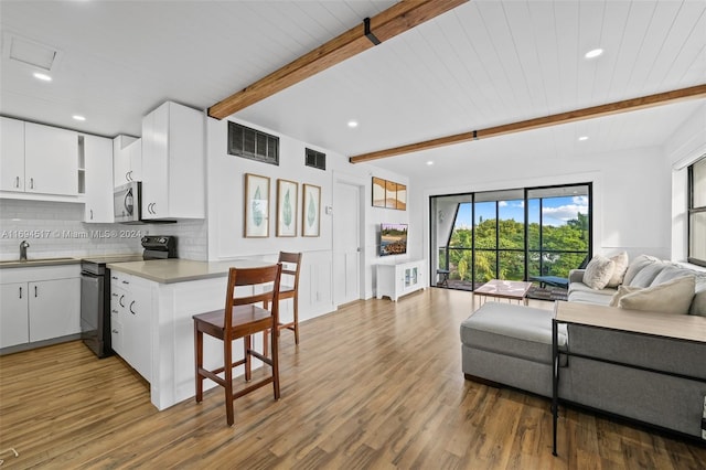 kitchen with hardwood / wood-style floors, white cabinets, black range with electric stovetop, beamed ceiling, and kitchen peninsula