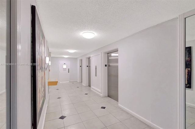 corridor with light tile patterned floors, a textured ceiling, and elevator