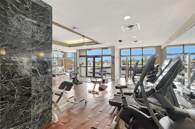 gym featuring hardwood / wood-style floors, expansive windows, a raised ceiling, and french doors