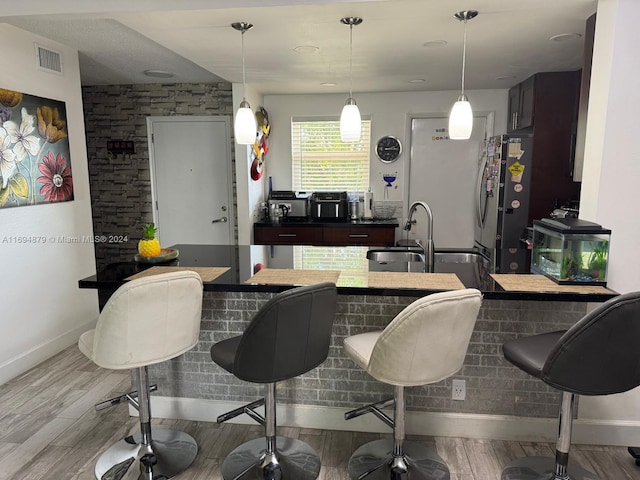 kitchen featuring a breakfast bar, sink, stainless steel fridge, light hardwood / wood-style floors, and dark brown cabinetry