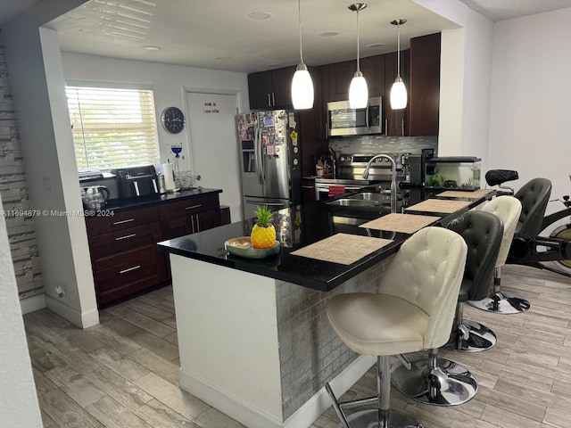 kitchen with pendant lighting, a kitchen breakfast bar, light hardwood / wood-style flooring, appliances with stainless steel finishes, and tasteful backsplash