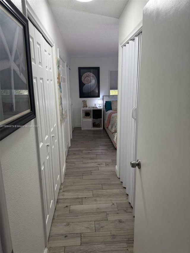 hall featuring light wood-type flooring and a textured ceiling