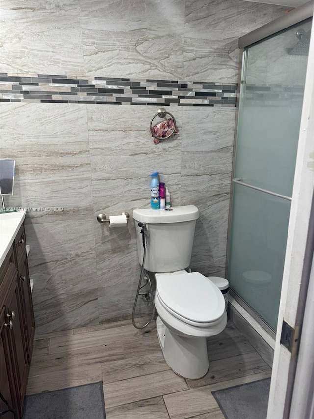 bathroom with vanity, toilet, a shower with door, and tile walls