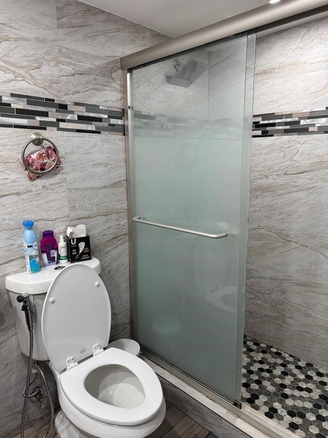 bathroom with a shower with shower door, tile walls, and toilet