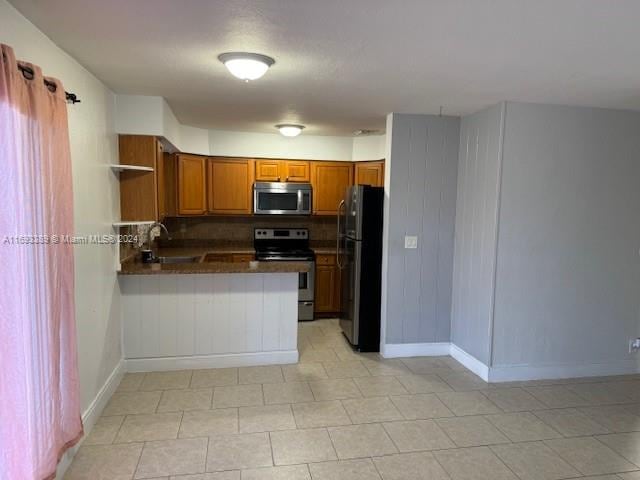 kitchen with decorative backsplash, kitchen peninsula, stainless steel appliances, and light tile patterned floors