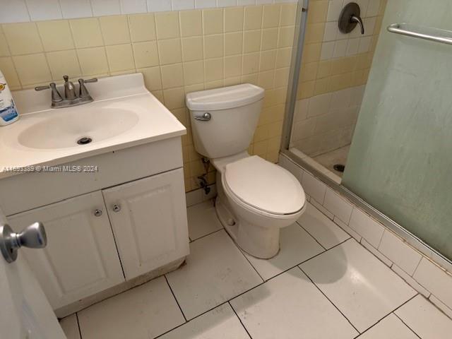 bathroom featuring walk in shower, tile patterned floors, toilet, vanity, and tile walls