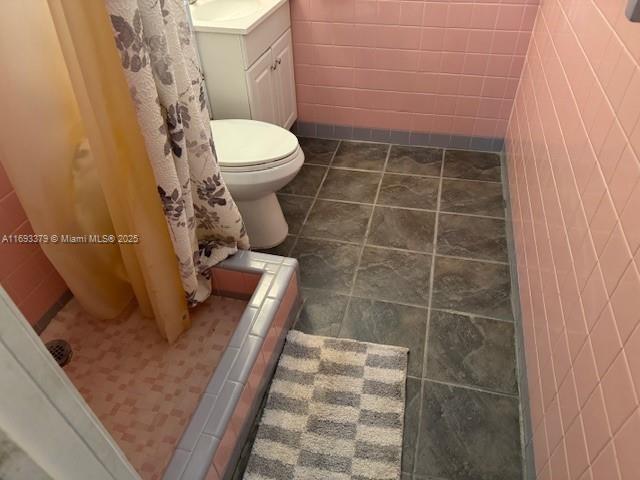 full bathroom with toilet, tile walls, curtained shower, and vanity