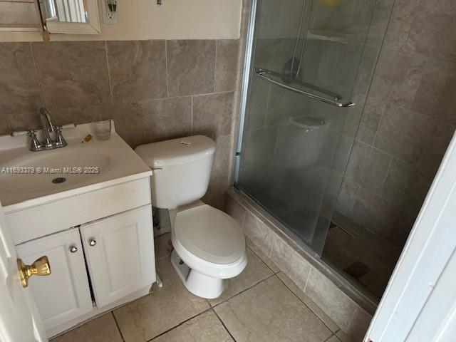 full bathroom with vanity, a stall shower, toilet, and tile walls