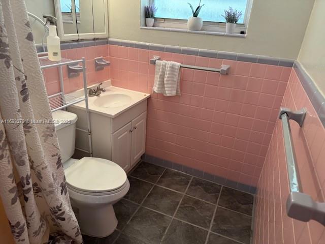 full bathroom featuring tile patterned flooring, vanity, wainscoting, toilet, and tile walls
