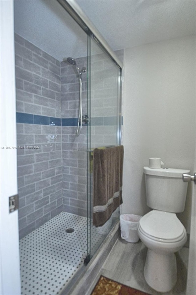 bathroom featuring a shower with door and toilet