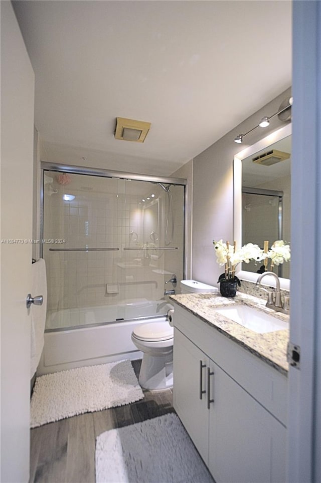 full bathroom with toilet, vanity, wood-type flooring, and combined bath / shower with glass door