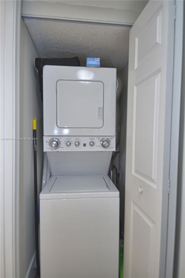 clothes washing area with a textured ceiling and stacked washer / dryer