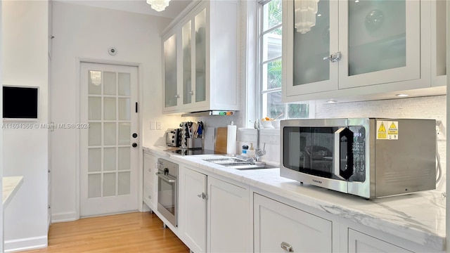 kitchen featuring light stone countertops, light hardwood / wood-style floors, decorative backsplash, white cabinets, and appliances with stainless steel finishes