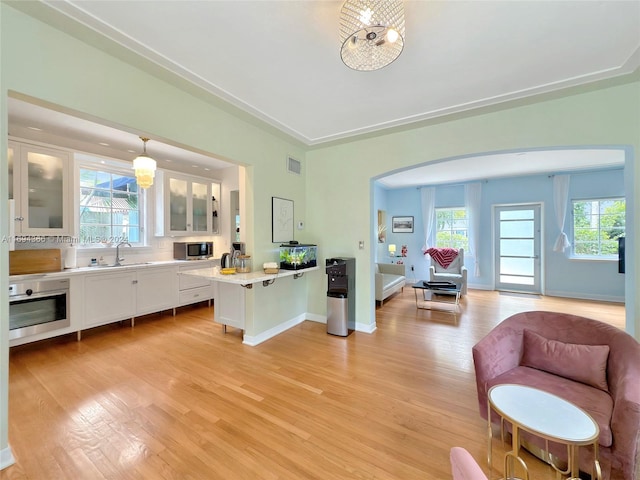 kitchen featuring stainless steel appliances, pendant lighting, light hardwood / wood-style flooring, white cabinets, and plenty of natural light