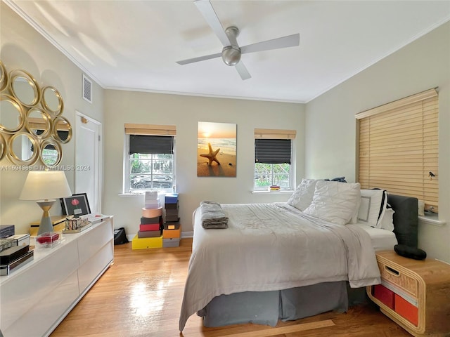 bedroom featuring ceiling fan, light wood-type flooring, ornamental molding, and multiple windows