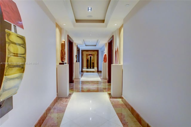 hall with light tile patterned floors and a raised ceiling