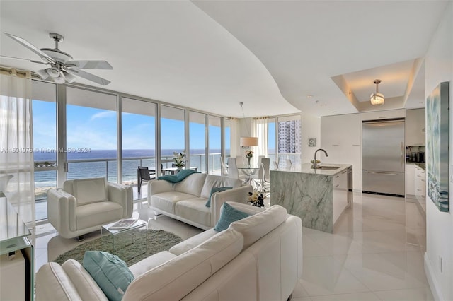 living room featuring floor to ceiling windows, ceiling fan, sink, light tile patterned floors, and a water view