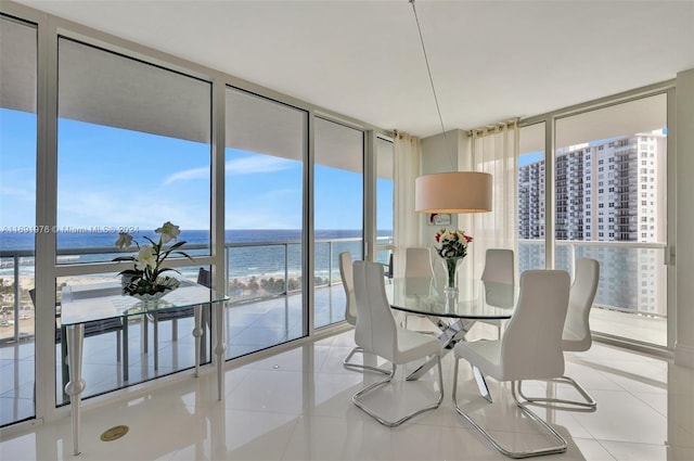 tiled dining room featuring a view of the beach, a water view, and expansive windows