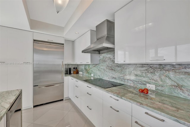 kitchen with wall chimney range hood, built in fridge, black electric cooktop, decorative backsplash, and white cabinets