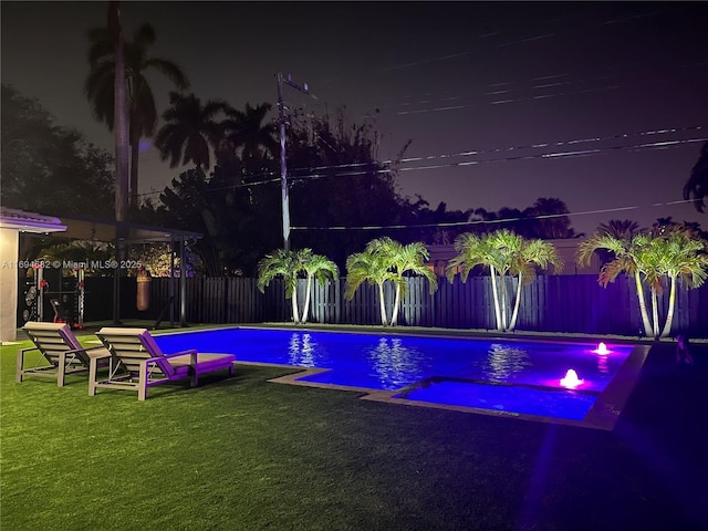 pool at night featuring a lawn