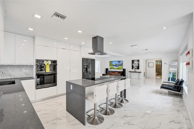 kitchen with island range hood, a kitchen breakfast bar, white cabinets, dark stone counters, and black appliances