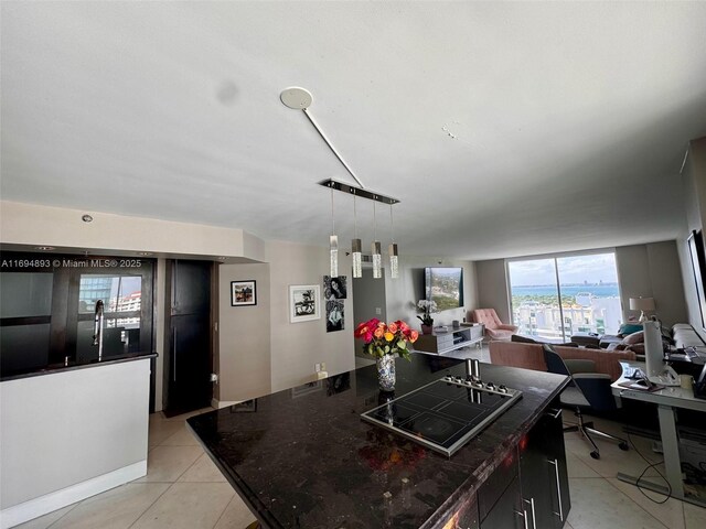 kitchen with a center island, dark stone counters, hanging light fixtures, light tile patterned flooring, and cooktop