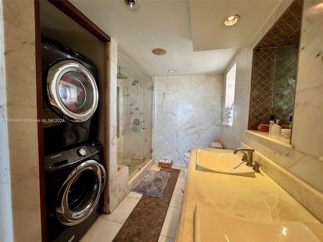 laundry area with light tile patterned floors, tile walls, stacked washer and clothes dryer, and sink