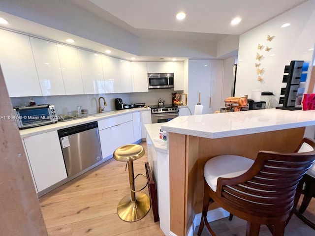 kitchen with white cabinets, a kitchen breakfast bar, sink, light wood-type flooring, and stainless steel appliances