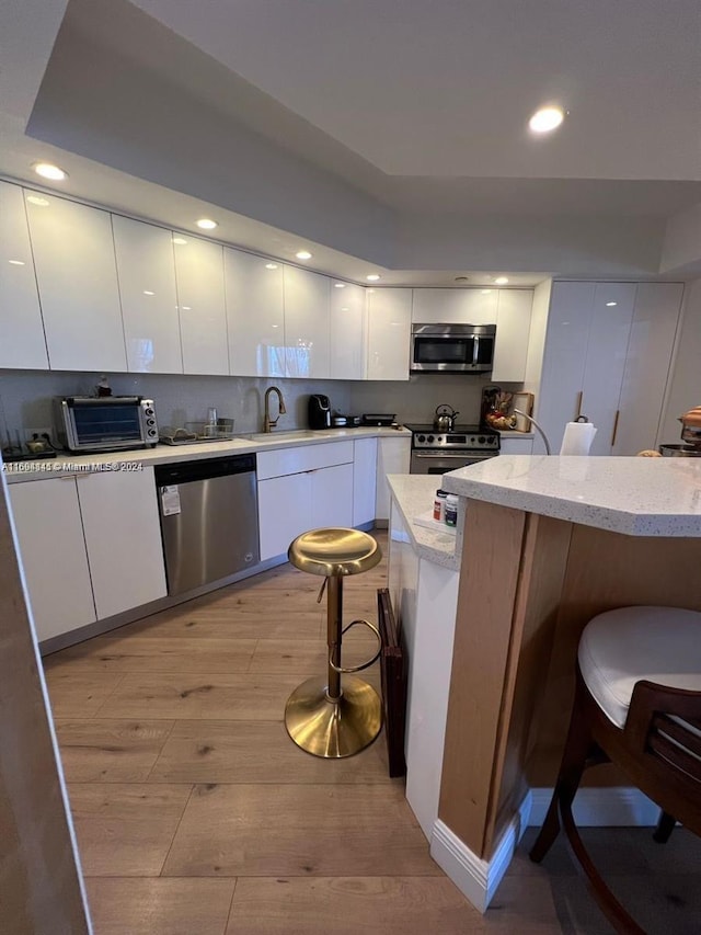 kitchen featuring a kitchen breakfast bar, white cabinets, stainless steel appliances, and light hardwood / wood-style floors