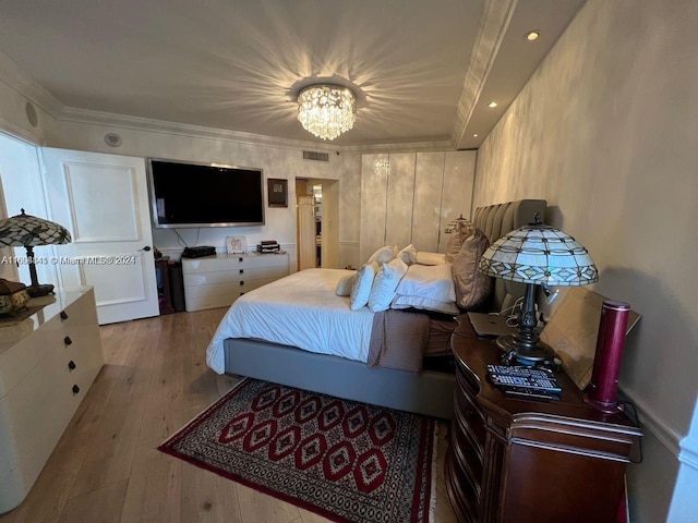 bedroom with an inviting chandelier, ornamental molding, and light wood-type flooring