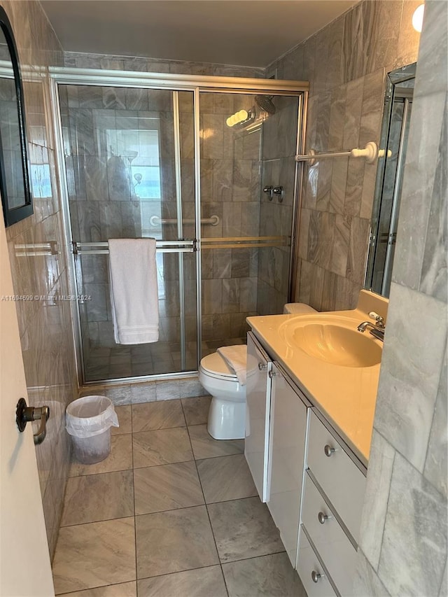 bathroom featuring vanity, tile patterned flooring, toilet, tile walls, and a shower with shower door